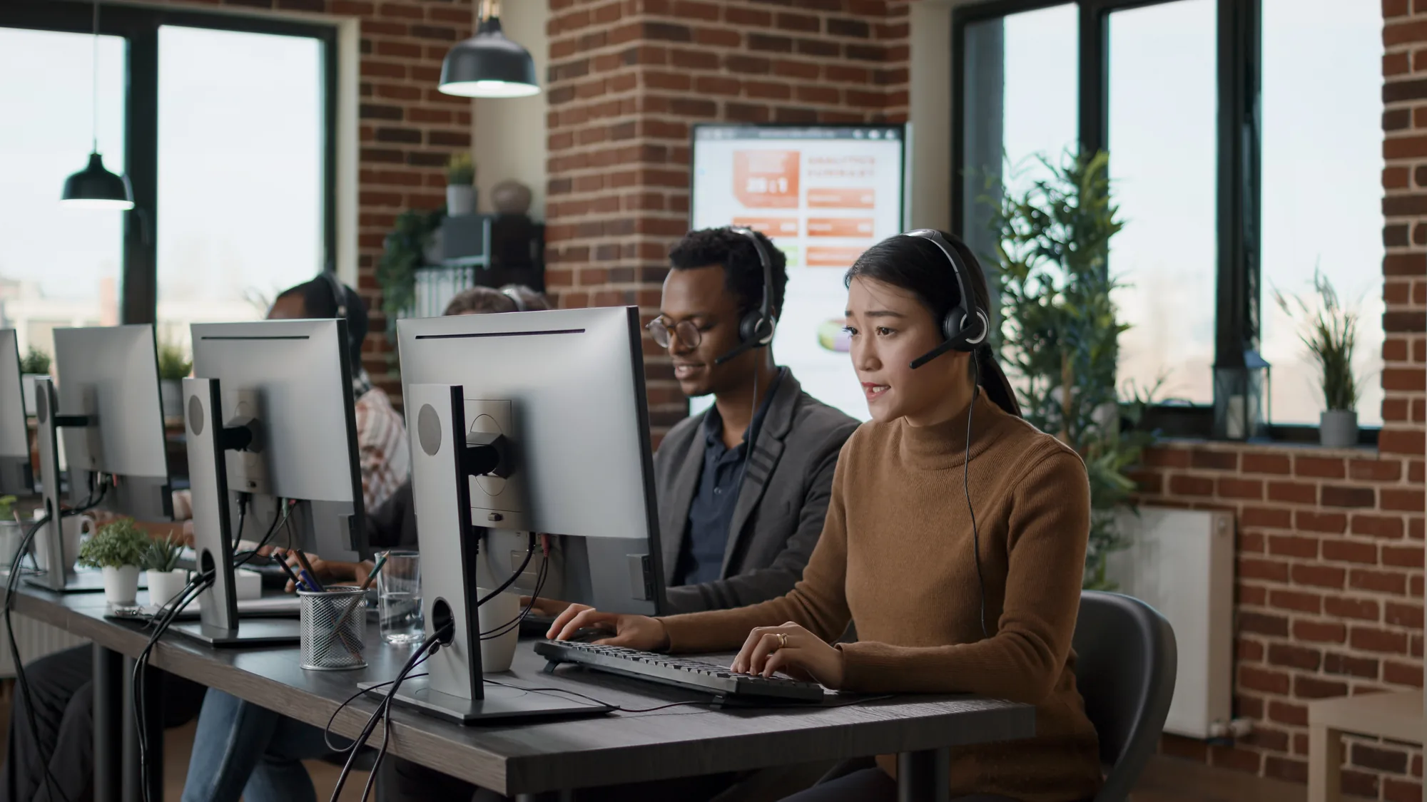 People at a row of desks wearing headsets, each at a monitor