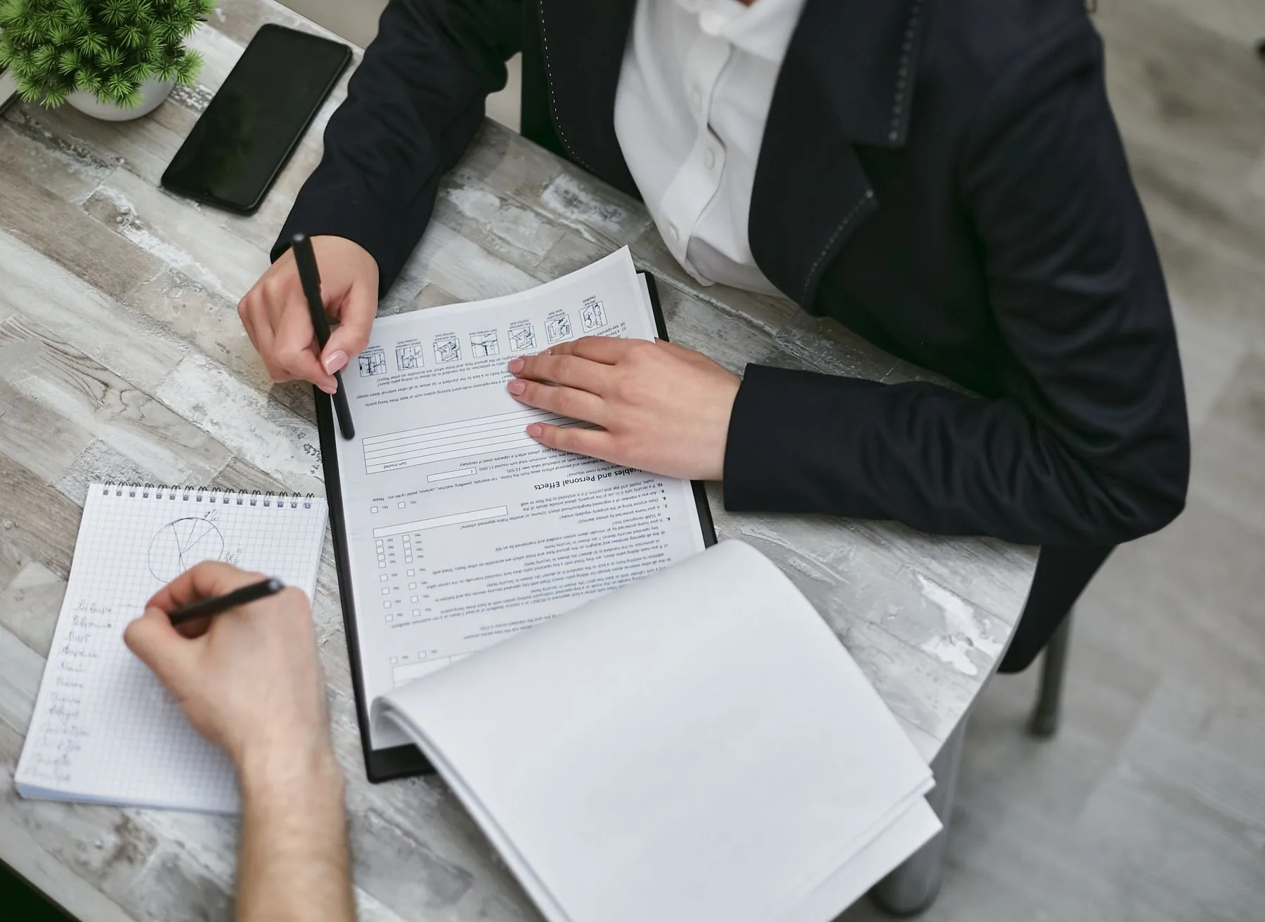 Two people at a desk going through a printed form, one pointing with a pen while the other takes notes